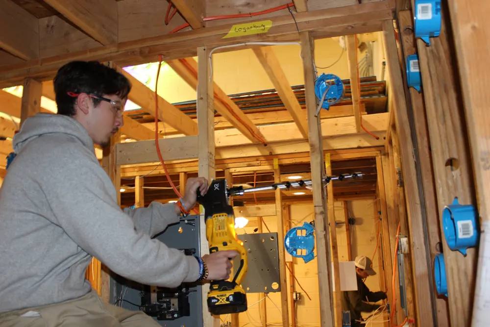 Student running wire in a wood frame construction